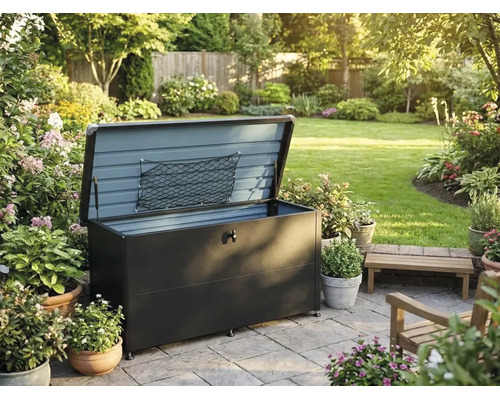 Garten-Auflagenbox aus Metall mit geöffnetem Deckel und Aufbewahrungsnetz auf einer gepflasterten Terrasse in einem Garten mit Pflanzen und Blumen.