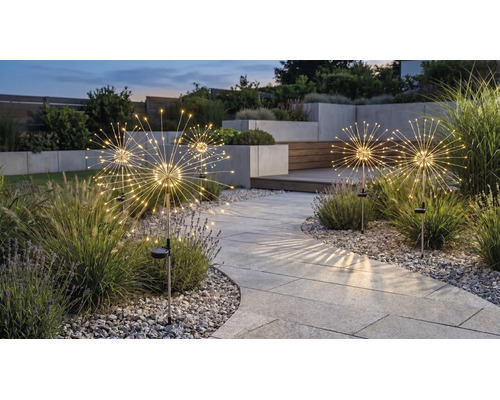 Solar-Gartenleuchten im Pusteblumen-Design mit Leuchtdioden entlang eines gepflasterten Weges in einem modern gestalteten Garten bei Dämmerung.