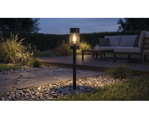 Solar-Gartenstecker mit LED-Leuchtmittel in Gitteroptik beleuchtet einen Gartenweg bei Nacht neben einer Lounge-Sitzecke.