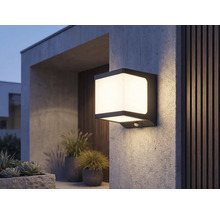 Moderne quadratische LED-Außenwandleuchte mit Bewegungsmelder, leuchtend an einer strukturierten Wand im Außenbereich.