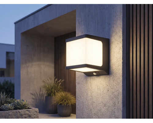 Moderne quadratische LED-Außenwandleuchte mit Bewegungsmelder, leuchtend an einer strukturierten Wand im Außenbereich.