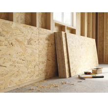 OSB-Platten an einer Holzwand in einem hellen Rohbau mit Hammer, Maßband und Schrauben auf dem Boden.