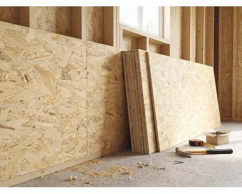 OSB-Platten an einer Holzwand in einem hellen Rohbau mit Hammer, Maßband und Schrauben auf dem Boden.