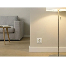 Moderne Wohnzimmerszene mit einer weißen Steckdose an der Wand, einer Stehleuchte, Holzboden und einem grauen Sofa im Hintergrund.