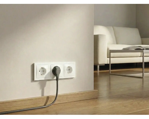 Dreifach-Steckdose mit eingestecktem Stecker an einer Wand über Holzboden in einem hellen Wohnzimmer.