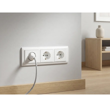 Dreifach-Steckdose mit eingestecktem Kabel an einer weißen Wand über einer Holzfußleiste in einem modern eingerichteten Raum.