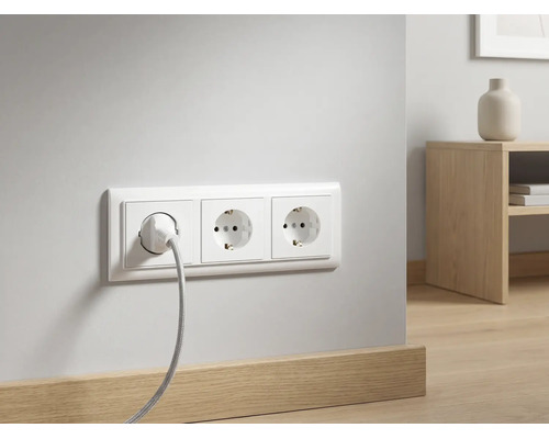Dreifach-Steckdose mit eingestecktem Kabel an einer weißen Wand über einer Holzfußleiste in einem modern eingerichteten Raum.