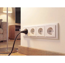 4-fach Schutzkontakt-Steckdose an einer hellen Wand im Wohnzimmer mit eingestecktem schwarzen Stecker einer Stehlampe.