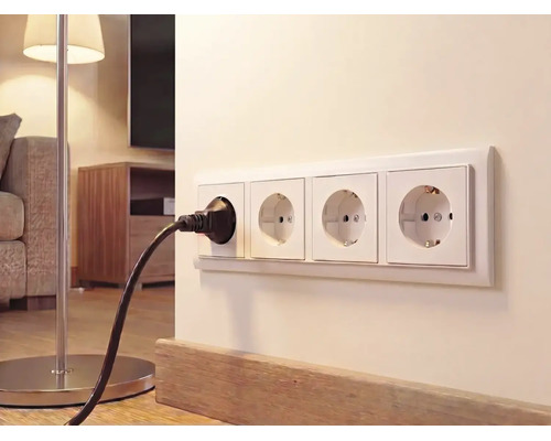 4-fach Schutzkontakt-Steckdose an einer hellen Wand im Wohnzimmer mit eingestecktem schwarzen Stecker einer Stehlampe.
