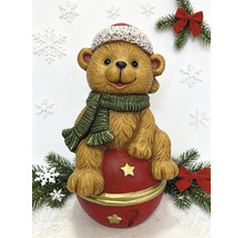 Weihnachtsfigur Teddybär auf einer Glocke mit Mütze und Schal zwischen Tannenzweigen und Schneeflocken.