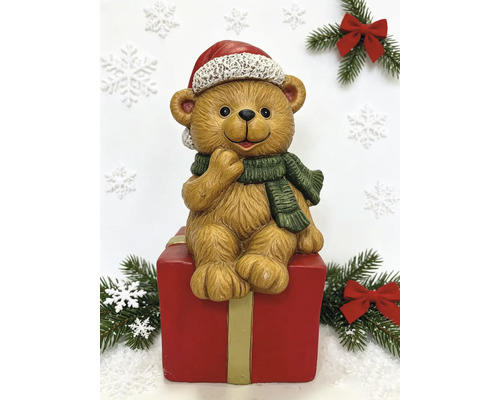Weihnachtsfigur Teddybär sitzend auf einer roten Geschenkbox mit Weihnachtsmütze und grünem Schal.