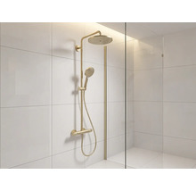 Duschsystem in Goldoptik mit Regendusche, Handbrause und Thermostatarmatur in einer hell gefliesten Dusche mit Glastrennwand.