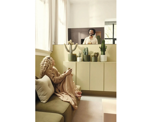 Helles Wohnzimmer mit Kakteen in Übertöpfen auf einem Sideboard, einer Frau auf dem Sofa und einem lachenden Mann im Hintergrund.
