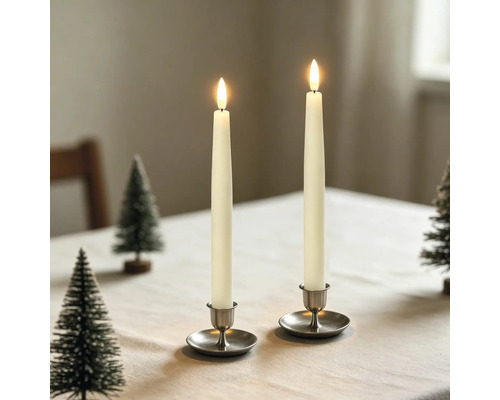 Zwei LED-Stabkerzen in Metallhaltern auf einem Tisch mit kleinen dekorativen Tannenbäumen.