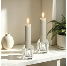 Zwei LED-Kerzen in würfelförmigen Glaskerzenhaltern auf einem hellen, organisierten Regal mit einer Vase und einer Pflanze.