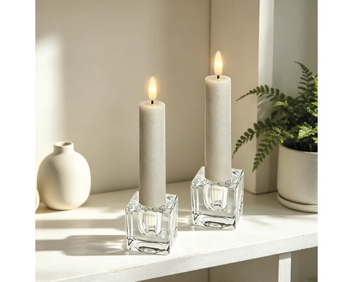 Zwei LED-Kerzen in würfelförmigen Glaskerzenhaltern auf einem hellen, organisierten Regal mit einer Vase und einer Pflanze.