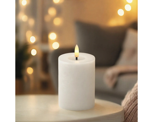 Weiße LED-Stumpenkerze auf einem Tisch vor einem unscharfen Hintergrund mit warmen Lichtern.
