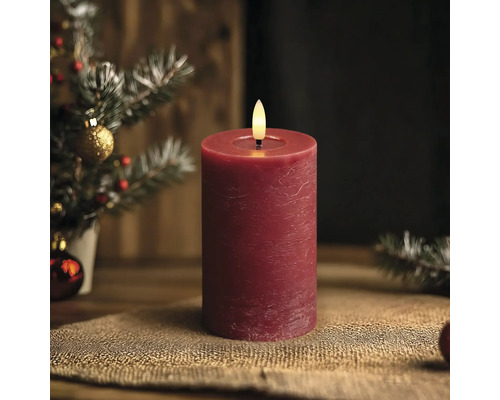 Rote LED-Stumpenkerze mit rustikaler Oberfläche vor einem weihnachtlichen Hintergrund.