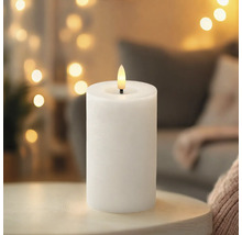 Weiße LED-Stumpenkerze mit flammenförmiger LED auf einem Tisch in wohnlicher Atmosphäre.