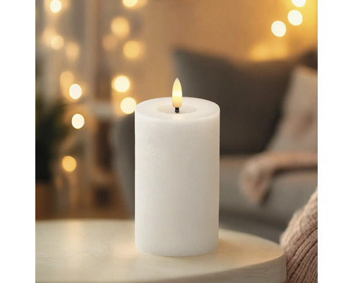 Weiße LED-Stumpenkerze mit flammenförmiger LED auf einem Tisch in wohnlicher Atmosphäre.