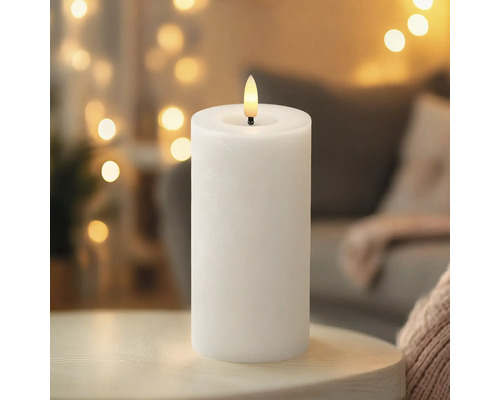 Weiße LED-Stumpenkerze mit realistischer Flamme auf einer Holzoberfläche vor einem Hintergrund mit unscharfen Lichtern.