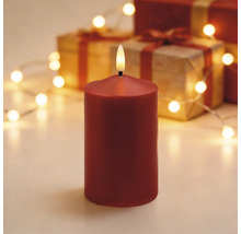 Rote LED-Stumpenkerze mit realistischer Flamme vor einem weihnachtlichen Hintergrund mit Geschenken und einer Lichterkette.