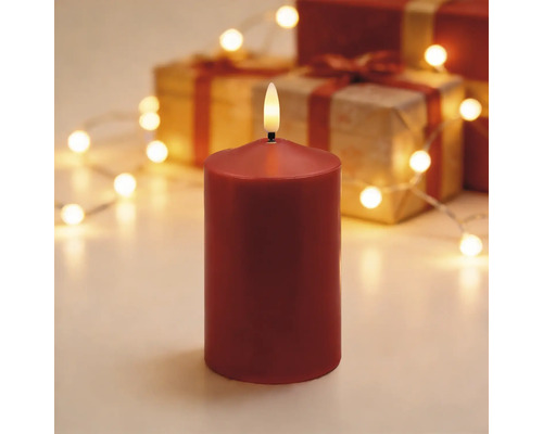 Rote LED-Stumpenkerze mit realistischer Flamme vor einem weihnachtlichen Hintergrund mit Geschenken und einer Lichterkette.