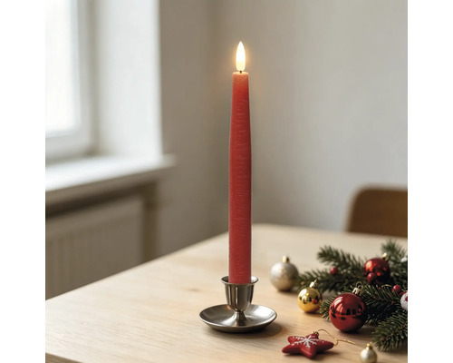 Rote LED-Stabkerze in einem Metallhalter auf einem Holztisch mit Weihnachtsdekoration aus Tannenzweigen und Christbaumkugeln.