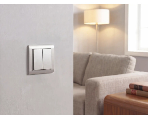 Moderner Doppel-Lichtschalter an einer Wand in einem hellen Wohnzimmer mit Sofa, Stehlampe und Holztisch.