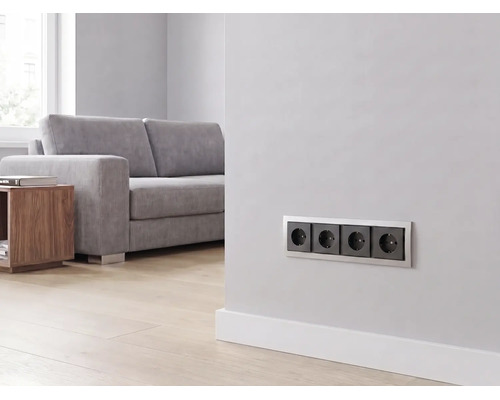 4-fach Steckdose installiert an einer Wand in einem hellen, modernen Wohnzimmer mit Sofa und Holzboden.