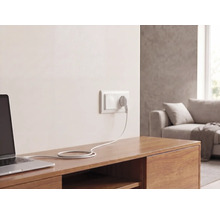 Wandsteckdose mit Stecker und Kabel, angeschlossen an einen Laptop auf einem Sideboard aus Holz in einem hellen Wohnzimmer.