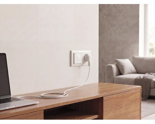 Wandsteckdose mit Stecker und Kabel, angeschlossen an einen Laptop auf einem Sideboard aus Holz in einem hellen Wohnzimmer.