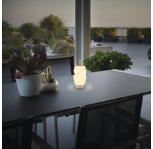 Moderne weiße LED-Tischleuchte im Spiraldesign auf einem dunklen Terrassentisch, umgeben von Topfpflanzen bei Dämmerung.