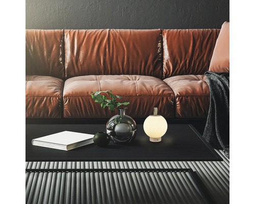 Modernes Wohnzimmer mit braunem Ledersofa, schwarzem Couchtisch und kleiner, leuchtender kugelförmiger Tischleuchte mit Tragegriff.