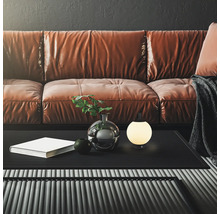 Moderne, kugelförmige Tischleuchte auf einem schwarzen Couchtisch vor einem braunen Ledersofa in einem stilvoll eingerichteten Wohnzimmer.