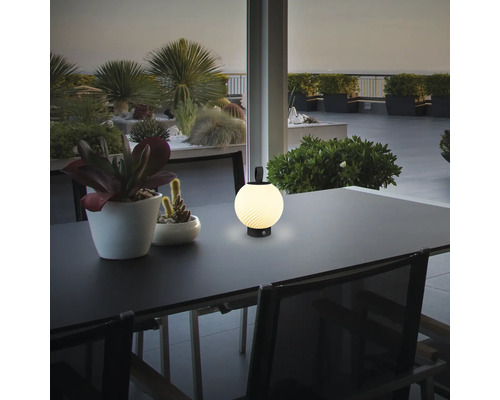 Tragbare LED-Außenleuchte auf einem Tisch, kugelförmig mit gerippter Oberfläche, in einer modernen Terrassenumgebung mit Pflanzen.