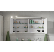 Spiegelschrank für das Bad mit LED-Beleuchtung, zwei offenen Türen, Glaseinlegeböden und Steckdose, befüllt mit Kosmetik vor einer Fliesenwand.