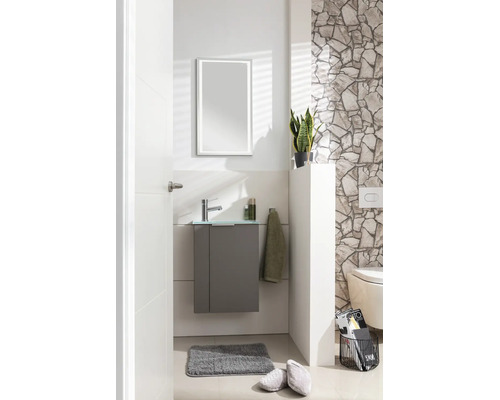 Modernes Gäste-WC mit grauem Unterschrank, Glaswaschbecken, Chromarmatur und LED-Spiegel vor einer hellen Wand mit Natursteinverblendern.