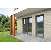 Fassade mit hellen Verblendsteinen in Klinkeroptik, bodentiefen Fenstern und einer Terrasse mit grauen Steinplatten.