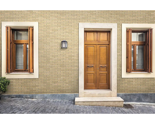 Außenfassade mit hellbeige Verblendern in Klinkeroptik, einer Holztür und Fenstern mit Fensterläden.
