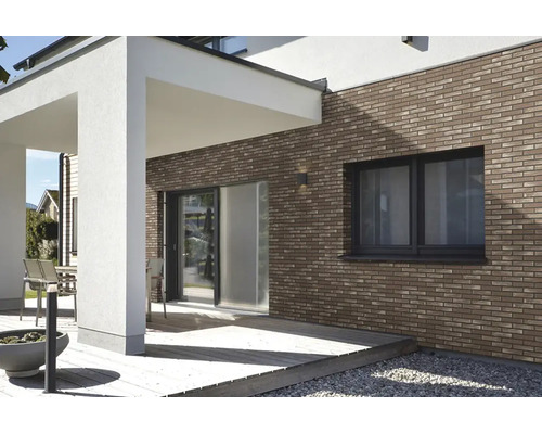 Moderne Hausfassade mit braunen Klinker-Riemchen an einer Terrasse mit Holzdeck und weißen Säulen.