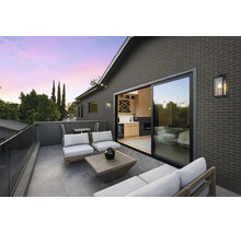 Moderne Dachterrasse mit grauer Klinkerfassade, Glasschiebetür, Lounge-Möbeln und Glasgeländer.