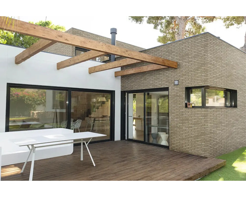 Moderne Terrasse mit Holzdeck, Klinkerfassade und Pergola aus Holzbalken.