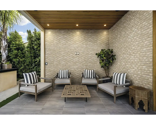 Überdachte Terrasse mit Verblendern in Steinoptik an den Wänden, Holzlamellendecke, grauen Bodenfliesen und modernen Gartenmöbeln.