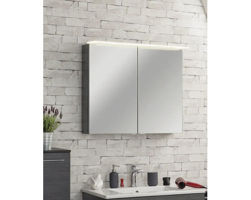 Spiegelschrank mit zwei Türen und LED-Beleuchtung an einer hellen Wand mit Steinoptik über einem Waschbecken im Badezimmer.