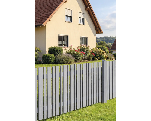 Grauer Lattenzaun aus Holz vor einem Wohnhaus mit Garten, der Rosen und Hortensien enthält.