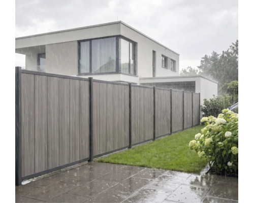 Moderner Sichtschutzzaun aus vertikalen Verbundwerkstoff-Paneelen bei Regen in einem Garten mit Rasen vor einem Wohnhaus.