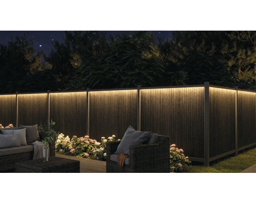 Beleuchteter Sichtschutzzaun im Garten bei Nacht mit LED-Lichtleiste, Gartenmöbeln und Pflanzen.