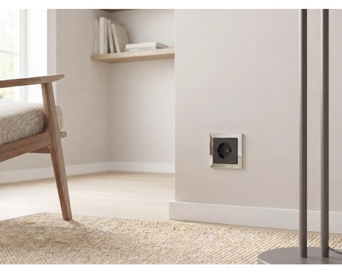 Schukosteckdose mit silbernem Rahmen und schwarzem Einsatz an einer hellen Wand in einem modernen Wohnzimmer.