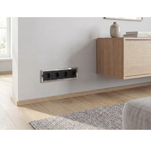 Schwarze 4-fach Steckdose mit verchromtem Rahmen, horizontal an einer hellen Wand in einem modernen Wohnzimmer montiert.